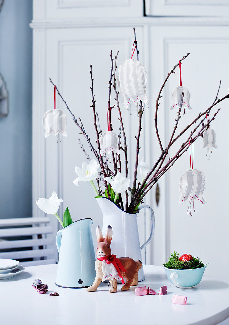 Äste mit Stoffblüten als Anhänger und weiße Tulpen in Kurgvase