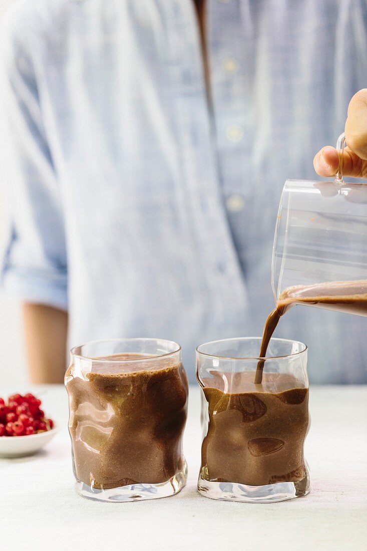 A woman pouring chocolate smoothie out of a jug into glasses
