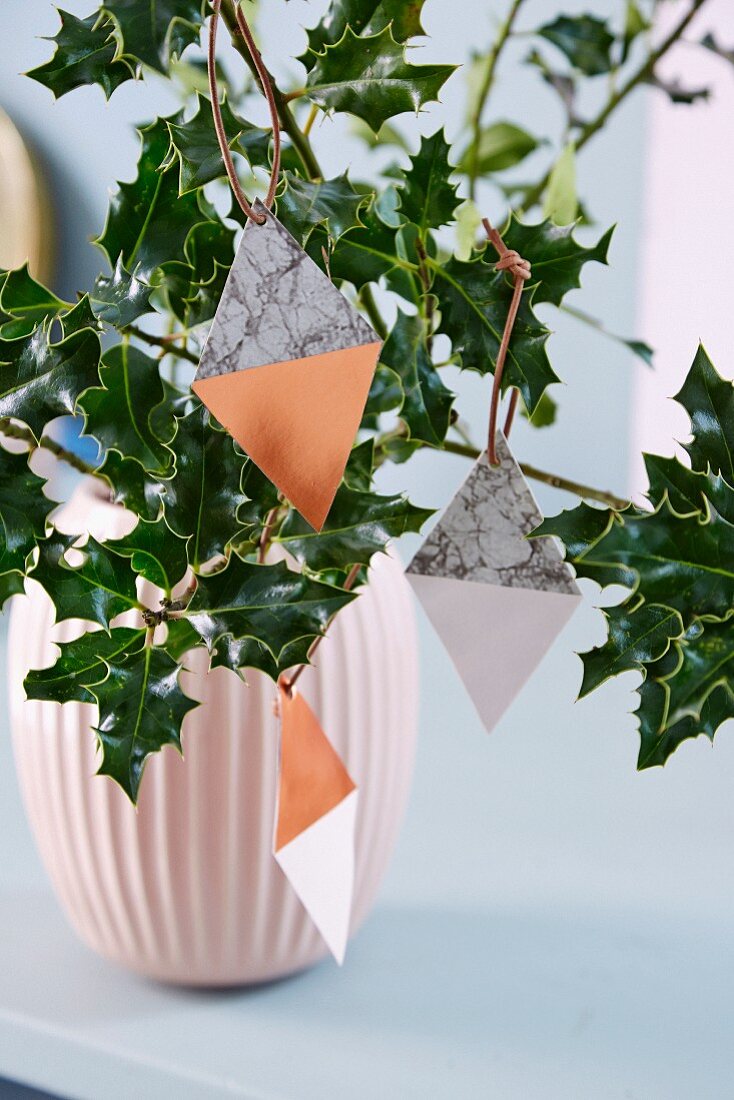 Diamond-shaped paper pendants hung from holly branches in vase