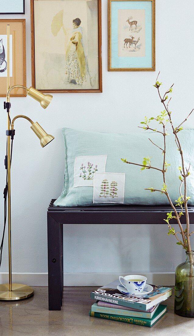 Cushion with embroidered panels on bench below gallery of pictures