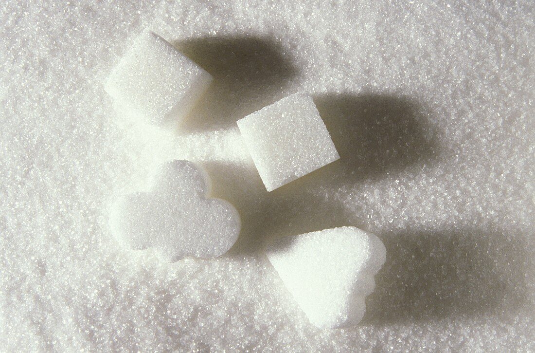 Vier verschiedene Zuckerwürfel auf Kristallzuckerboden