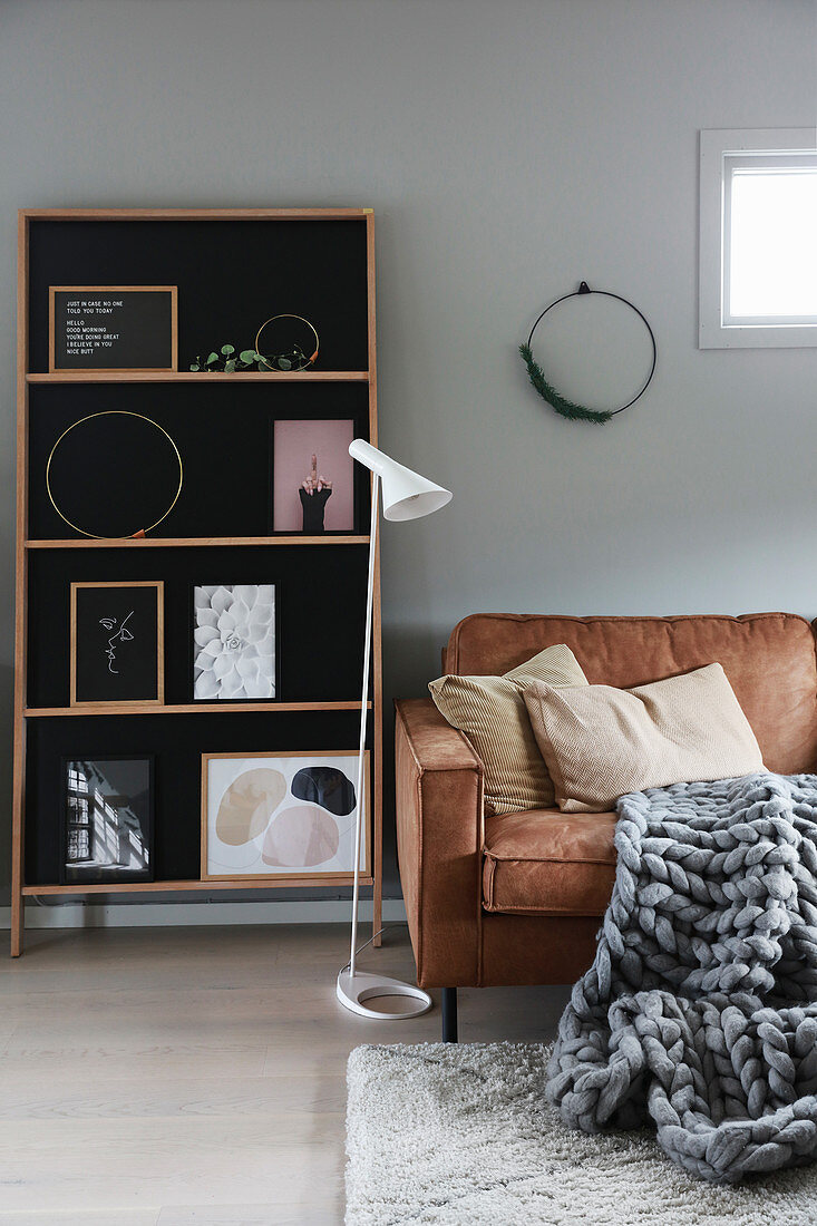 Scatter cushions and giant knit blanket on leather sofa, standard lamp and shelves