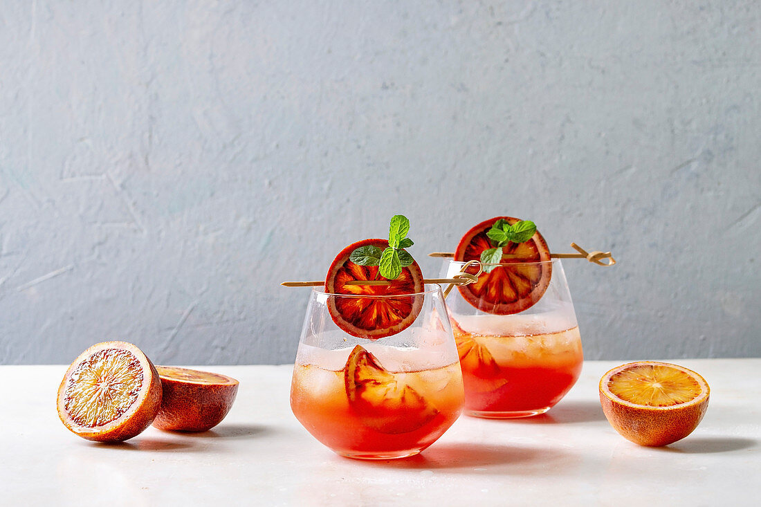 Blood orange iced cocktails in glasses, decorated by slice of oranges and fresh mint on skewers