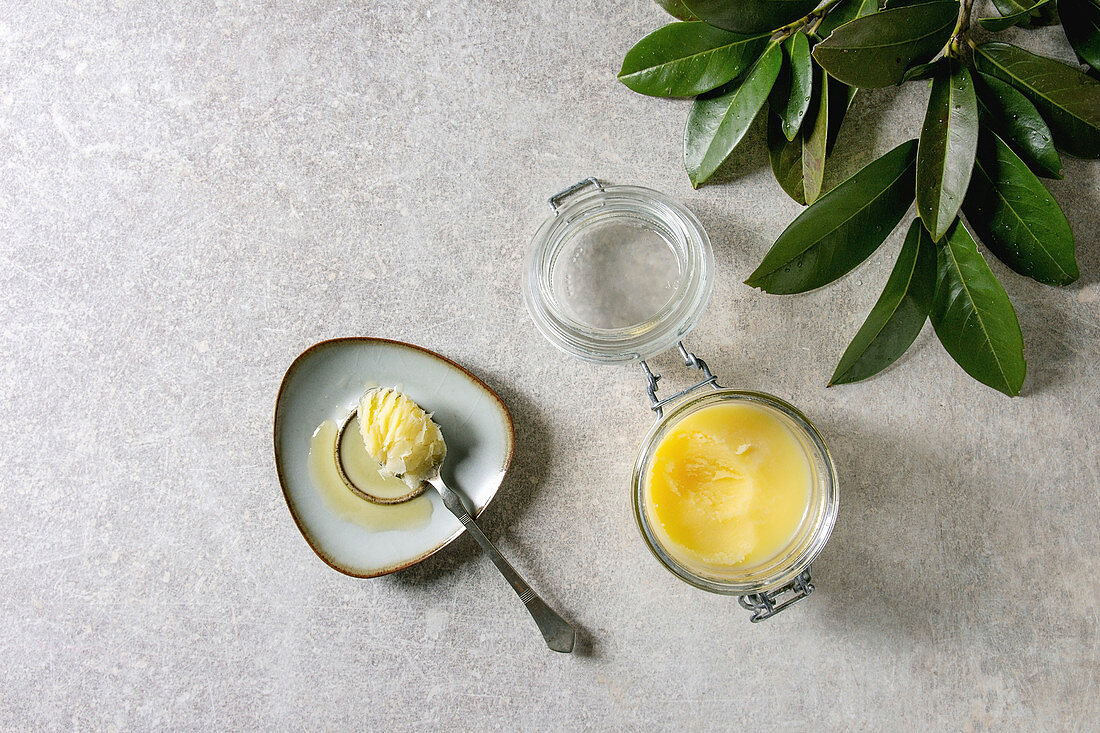 Homemade Melted ghee clarified butter in open glass jar and spoon on saucer