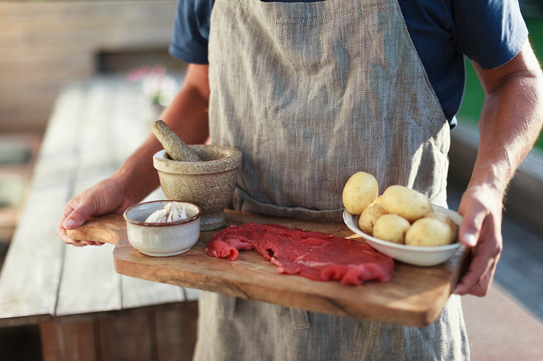 Man carrying cutting board with raw meat and potatoes