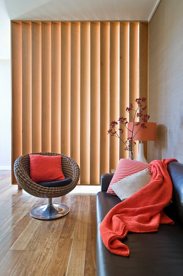 Designer armchair and leather sofa in living room with slatted wooden partition in background