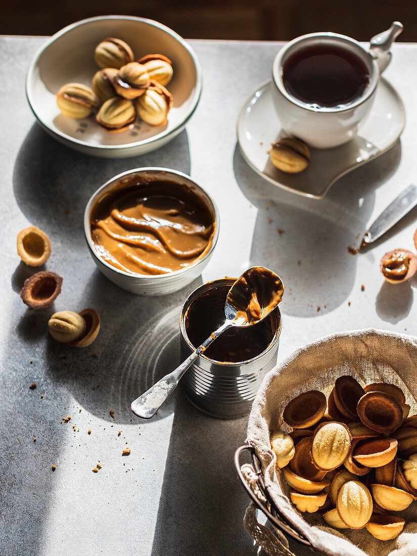 Walnut cookies in a basket with dulce de leche in a bowl and tea cup on gray background