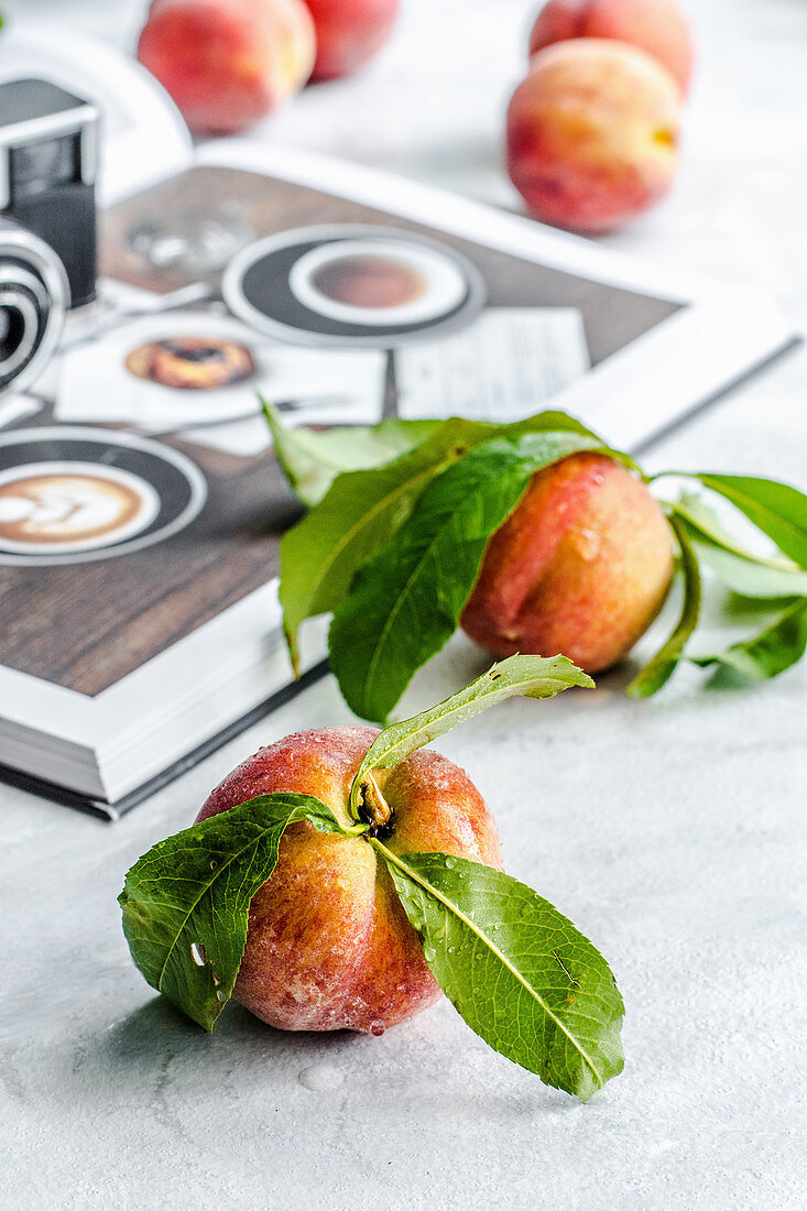 Frische Pfirsiche mit Blättern neben Buch und Fotoapparat