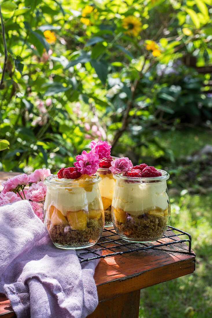 Summer dessert in the garden served in jars, prepared from crushed cookies, peaches, vanilla cream and fresh raspberries