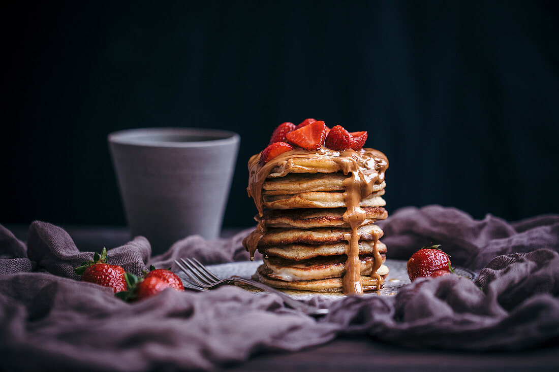 Stack of pancakes topped with strawberries, peanut butter and maple syrup