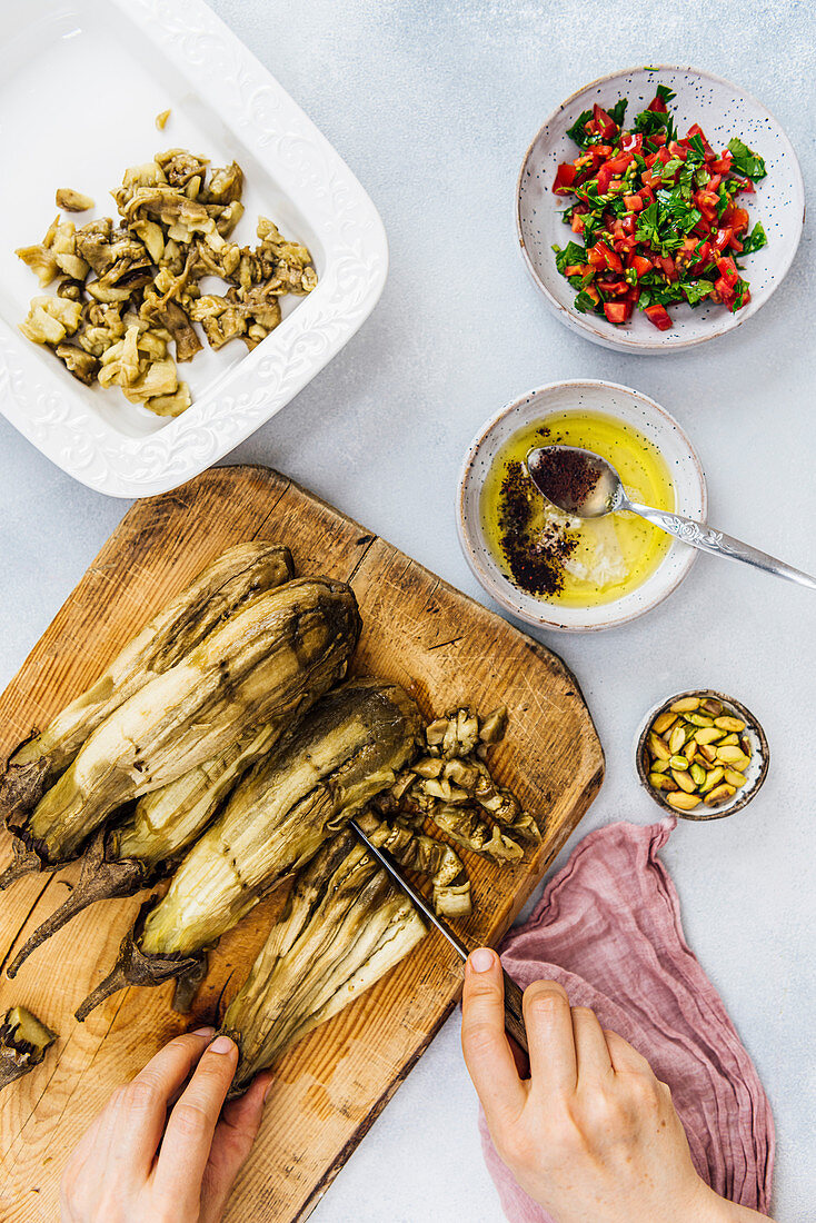 Woman chopping roasted eggplants on a wooden board to make Turkish eggplant salad