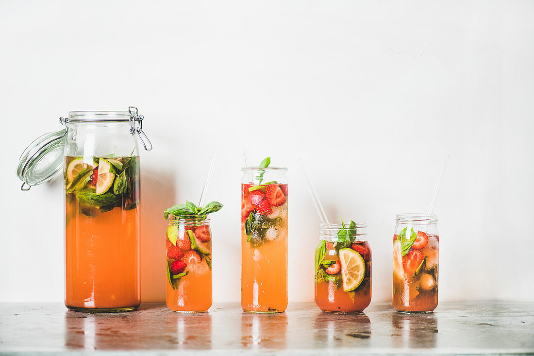 Homemade strawberry and basil lemonade or ice tea in glass tumblers with eco-friendly plastic-free straws on grey concrete table