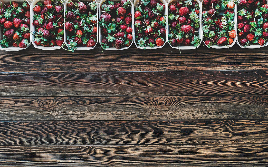 Frisch geerntete Erdbeeren in Pappschalen auf Holzuntergrund (Aufsicht)