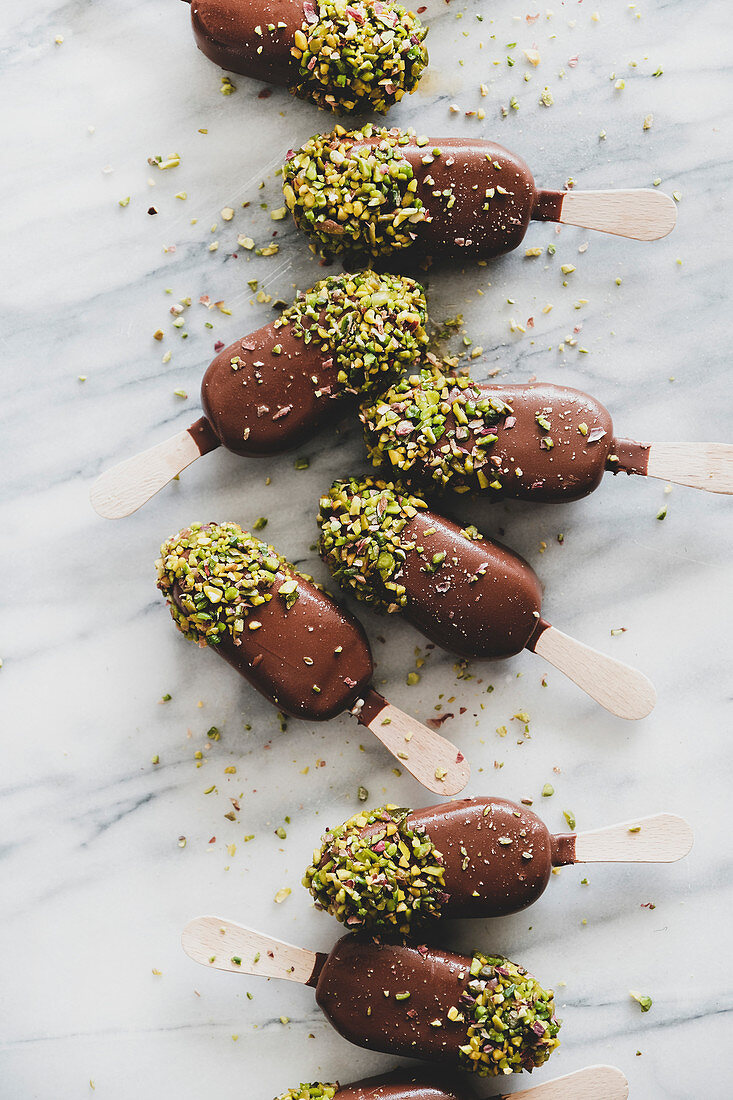Ice cream popsicle pattern: Flat-lay of chocolate glazed ice cream pops with pistachio icing over grey marble background