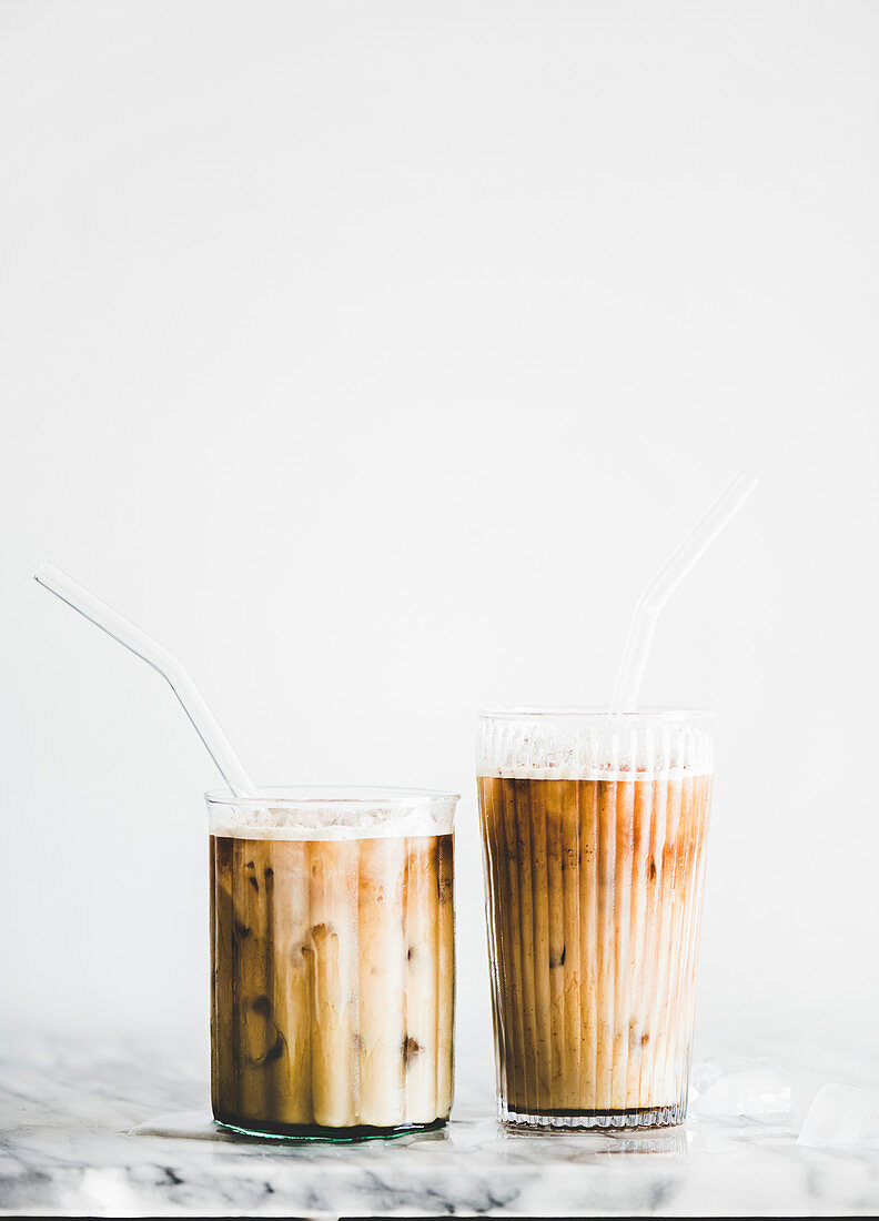 Homemade iced latte coffee in glasses with straws on marble table, white wall at background