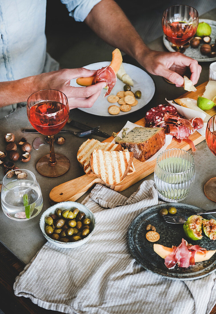 Charcuterie and cheese board, rose wine, nuts, olives, fresh fruits and mans hands with food