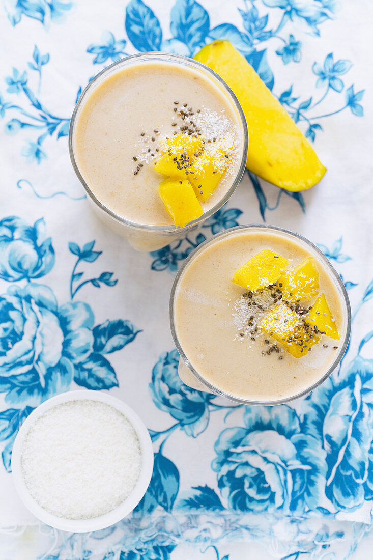 Mango-Bananen-Smoothie dekoriert mit Mangostückchen und Kokosraspeln