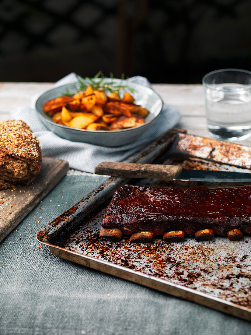 BBQ smoked glazed grilled pork ribs on rustic background with roasted potatoes and cereal bread