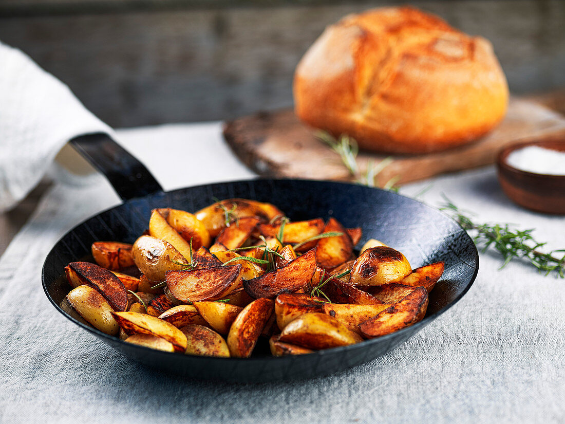Roasted potato wedges with rosemary in a wrought iron pan on a tablecloth