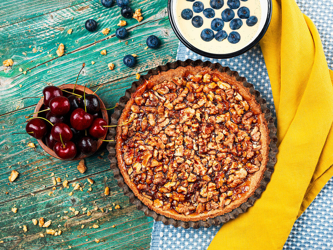 Walnusstarte in der Form, daneben Kirschen und Vanillesauce mit Blaubeeren