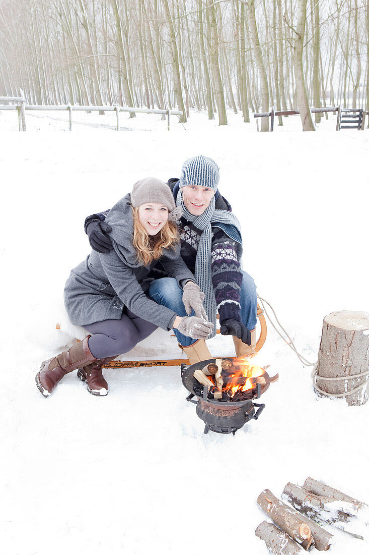 Pärchen wärmt sich die Hände am Grill im Schnee auf