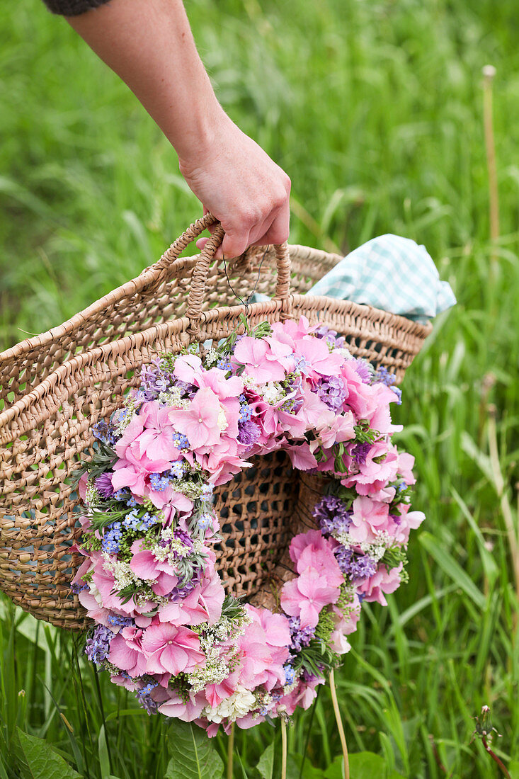Wreath of hydrangea florets, forget-me-nots and chive flowers on shopping basket