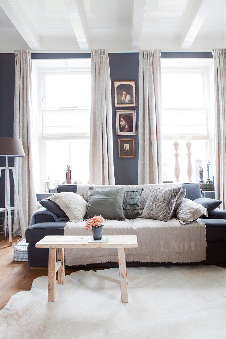 Sofa with scatter cushions and wooden bench used as coffee table in living room with grey walls