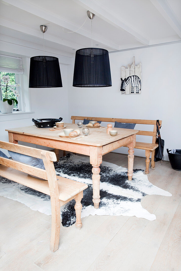 Wooden table and benches on cowhide rug below black pendant lamps