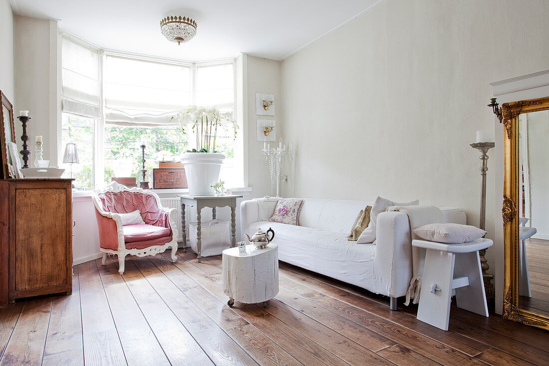 Weißes Hussensofa, Holztisch mit Orchideen und Sessel im Wohnzimmer mit dunklem Dielenboden