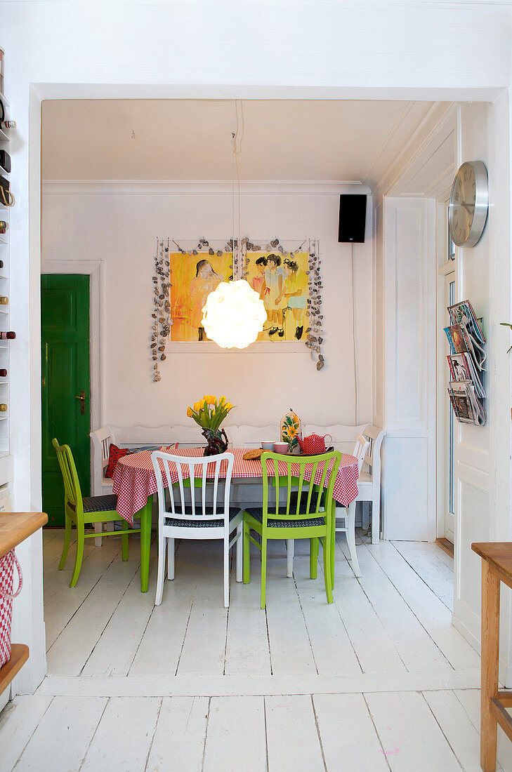 Green and white spoke-back chairs and bench at dining table on white floorboards