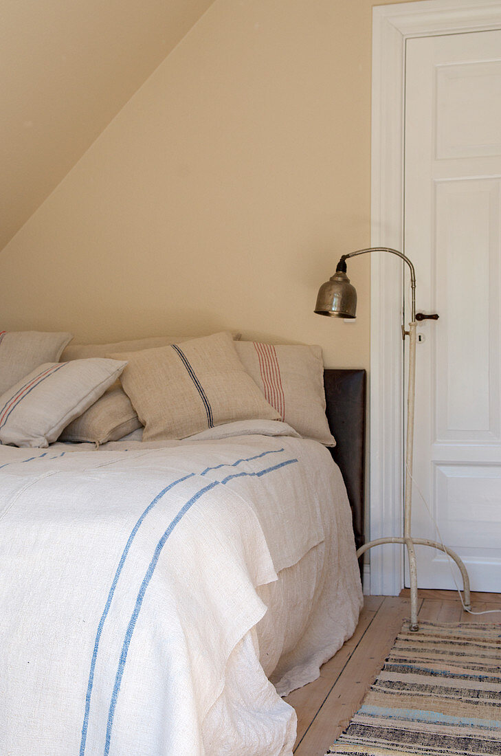 Floor lamp next to the bed with bed linen under the eaves