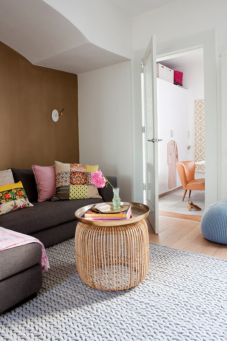 Grey sofa with colourful scatter cushions against brown wall and drum-shaped coffee table in living room