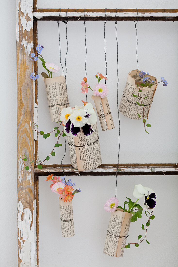 Flowers in glasses covered in book pages and hung in old window frame