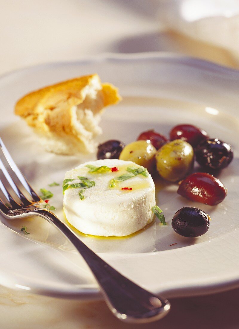 Kleiner Ziegenfrischkäse mit Oliven & Weißbrot auf Teller
