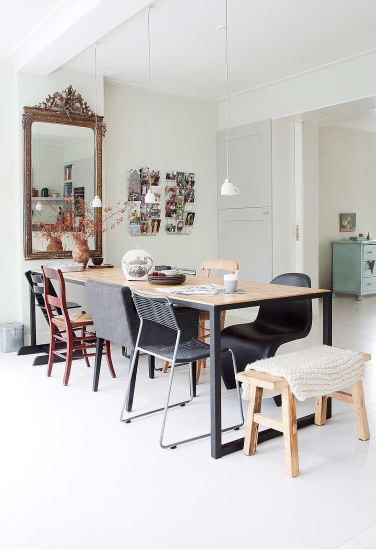 Long dining table with various chairs and antique mirror in bright dining area