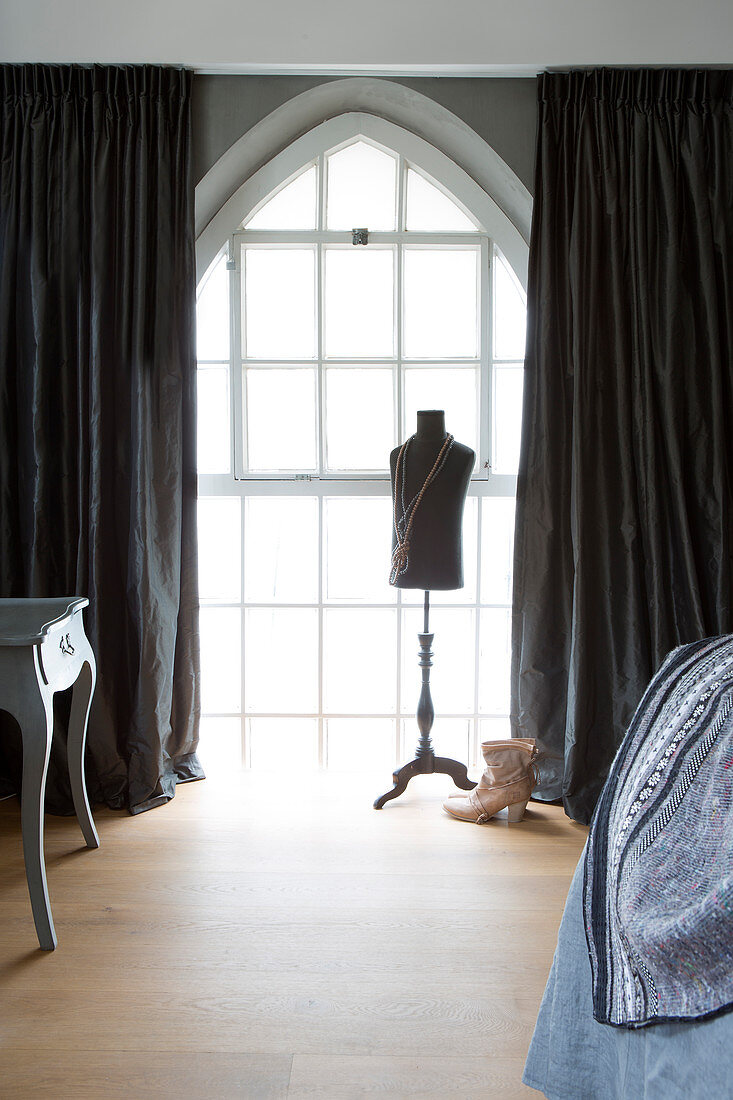 Tailors' dummy in front of arched lattice window with dark curtains