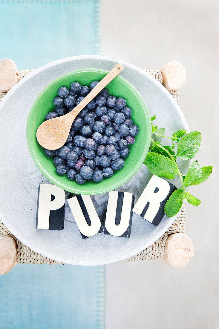 Fresh blueberries with wooden spoon in a bowl on a stool