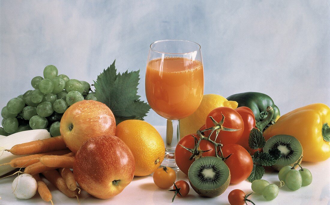 Glas mit Multivitaminsaft umgeben von frischem Gemüse & Obst