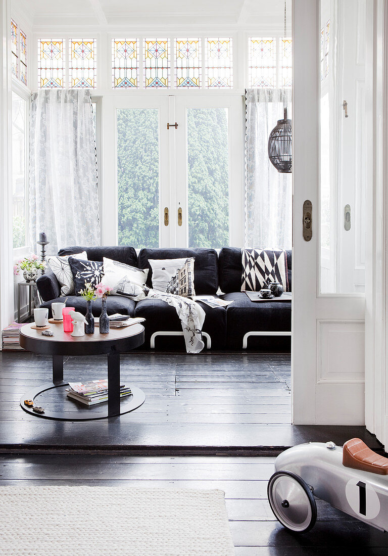 A view into the living room with a black sofa and coffee table in front of a window