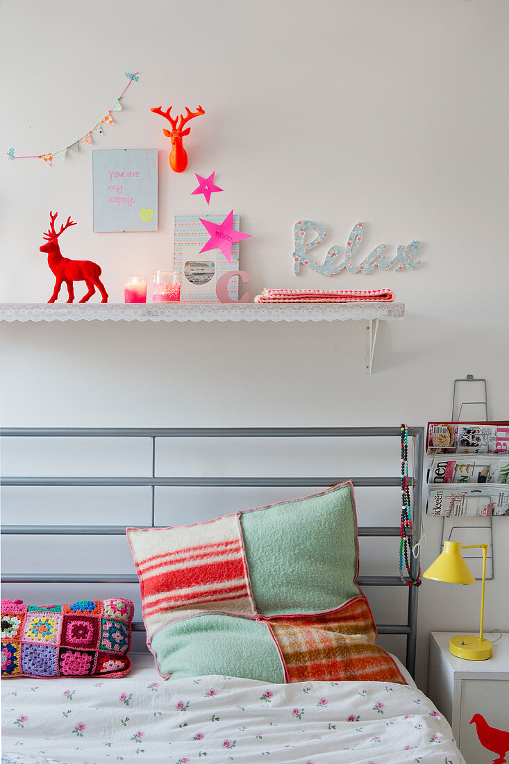 Colourful accessories on shelf above bed with handmade cushions