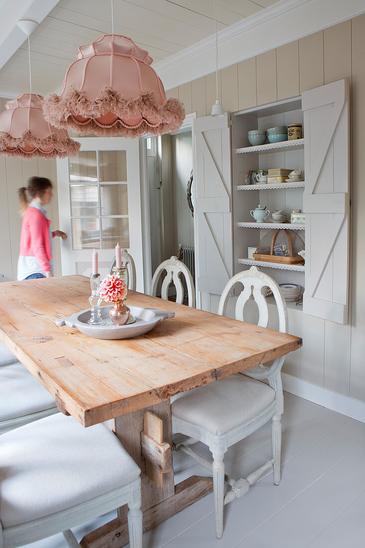 Old-fashioned lights above a rustic dining table in front of built in shelves