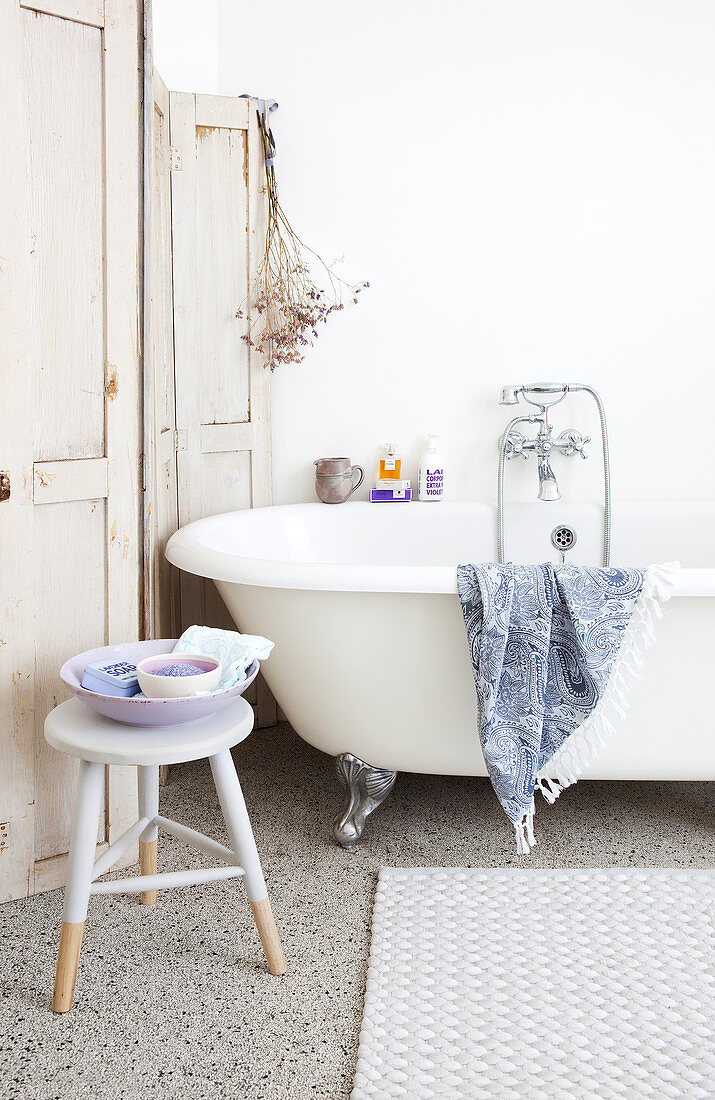 Stool in front of the free-standing bathtub and a privacy screen with worn paint