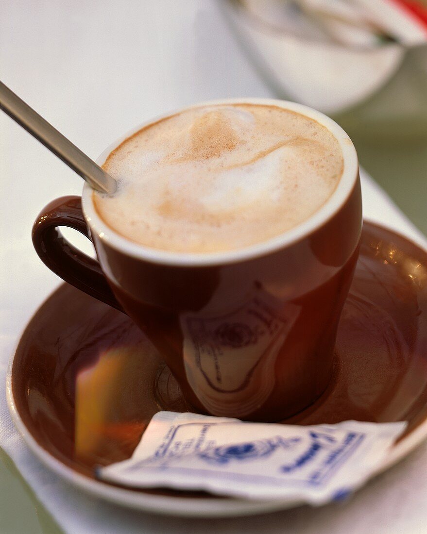 Cappuccino in brauner Tasse mit Löffel & Zucker