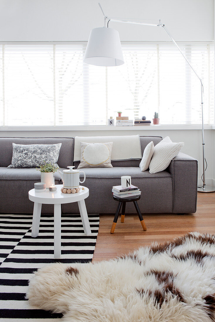 Pale grey sofa and standard lamp in front of window and side table on black-and-white striped rug