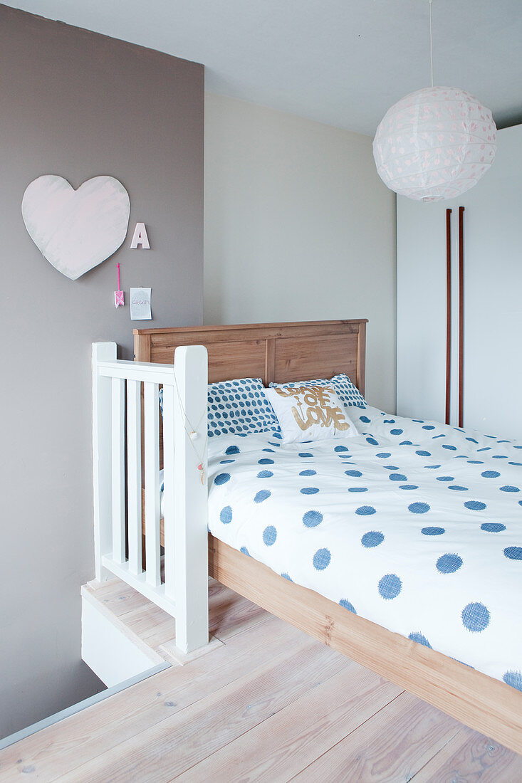 Blue polka-dot bed linen on wooden bed below pendant lamp with paper lampshade