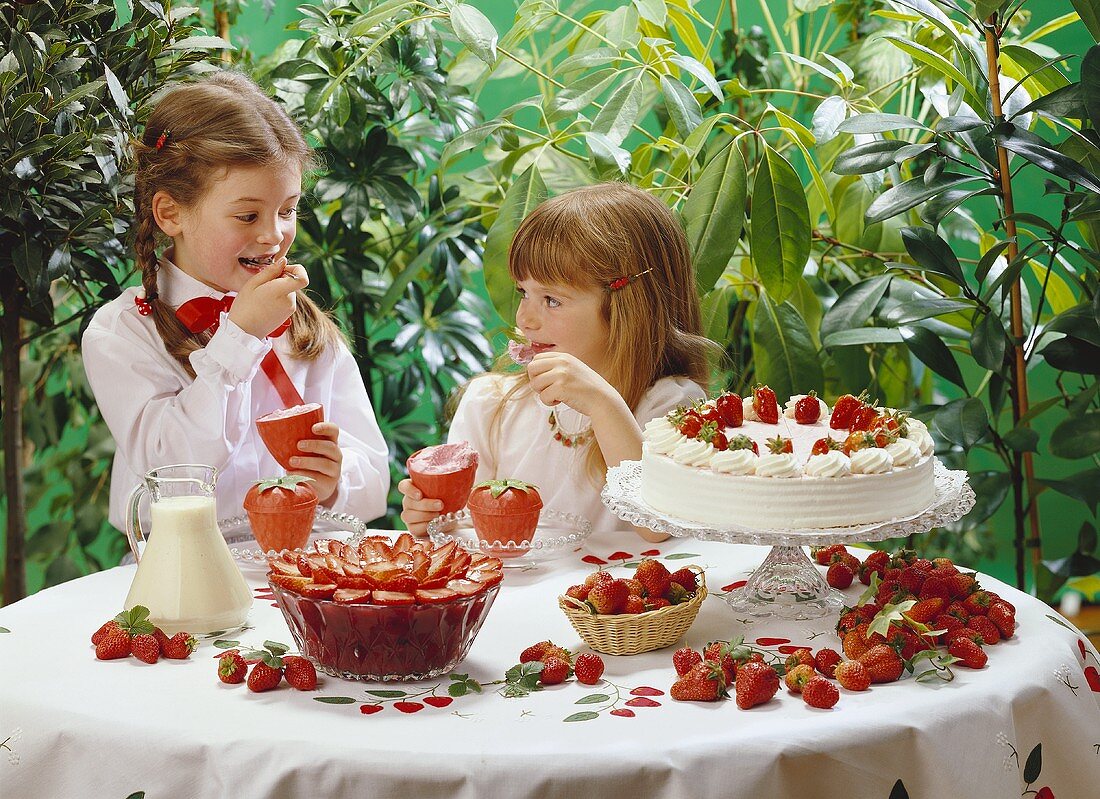 2 Mädchen am Tisch mit Erdbeerdesserts essen Erdbeercreme
