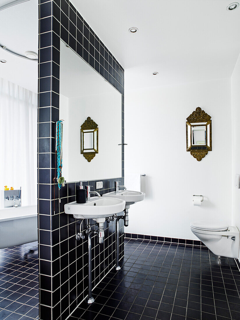 Sink and mirror on partition wall with black tiles