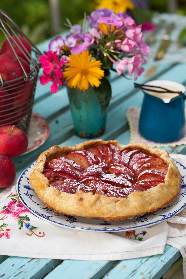 Homemade apple pie and vase of flowers on garden table