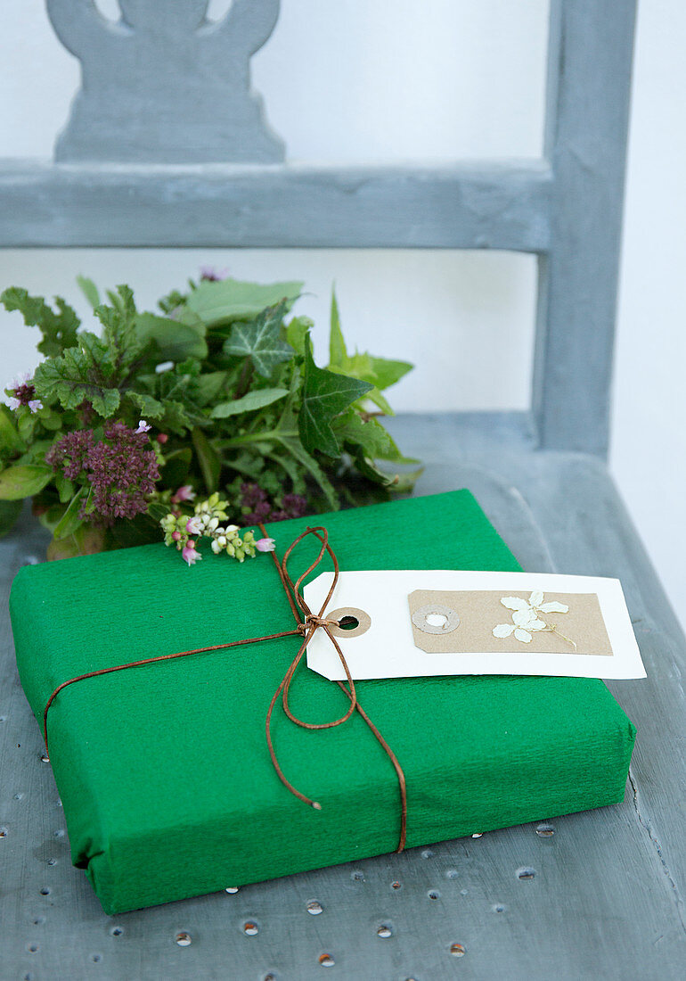 Grün verpacktes Geschenk mit Anhänger und Strauß aus dem Garten