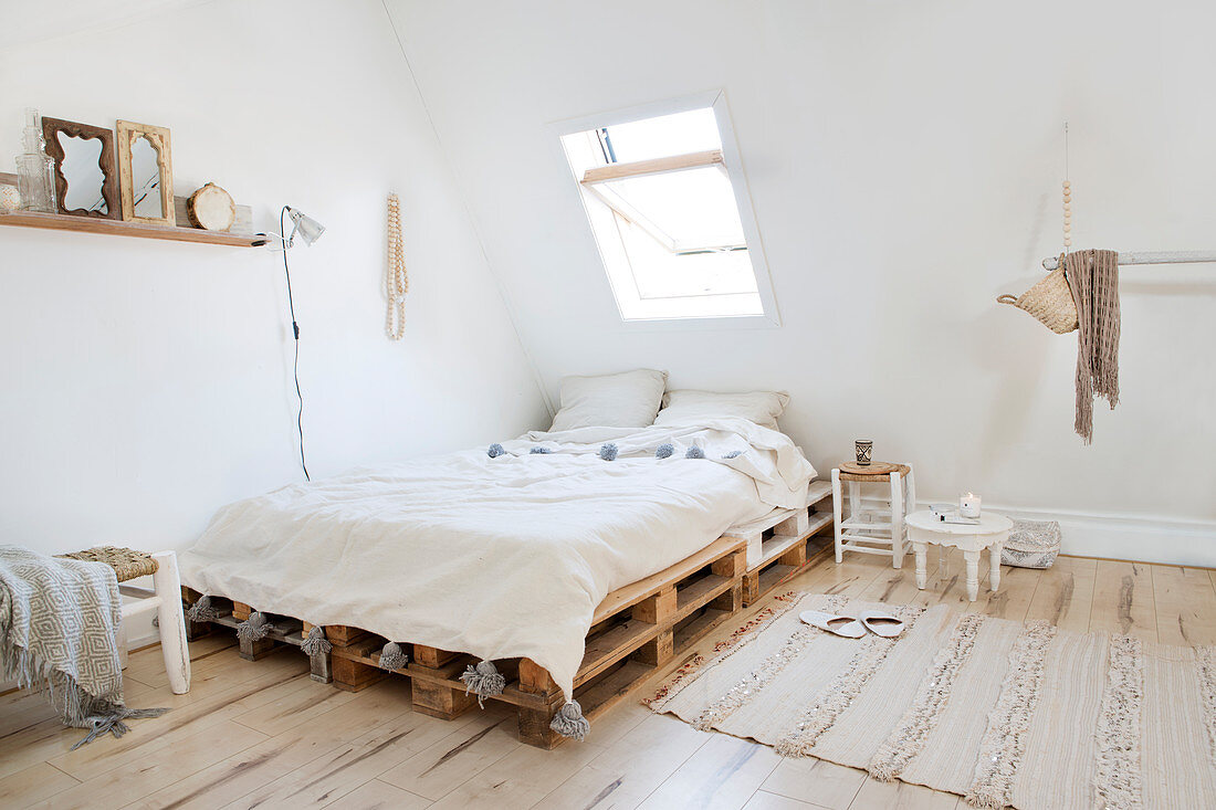 Bedroom in natural tones under the eaves of a sloping roof with pallet bed